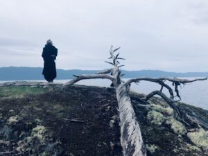 Denise looking out at the ocean beside twisted fallen tree trunk